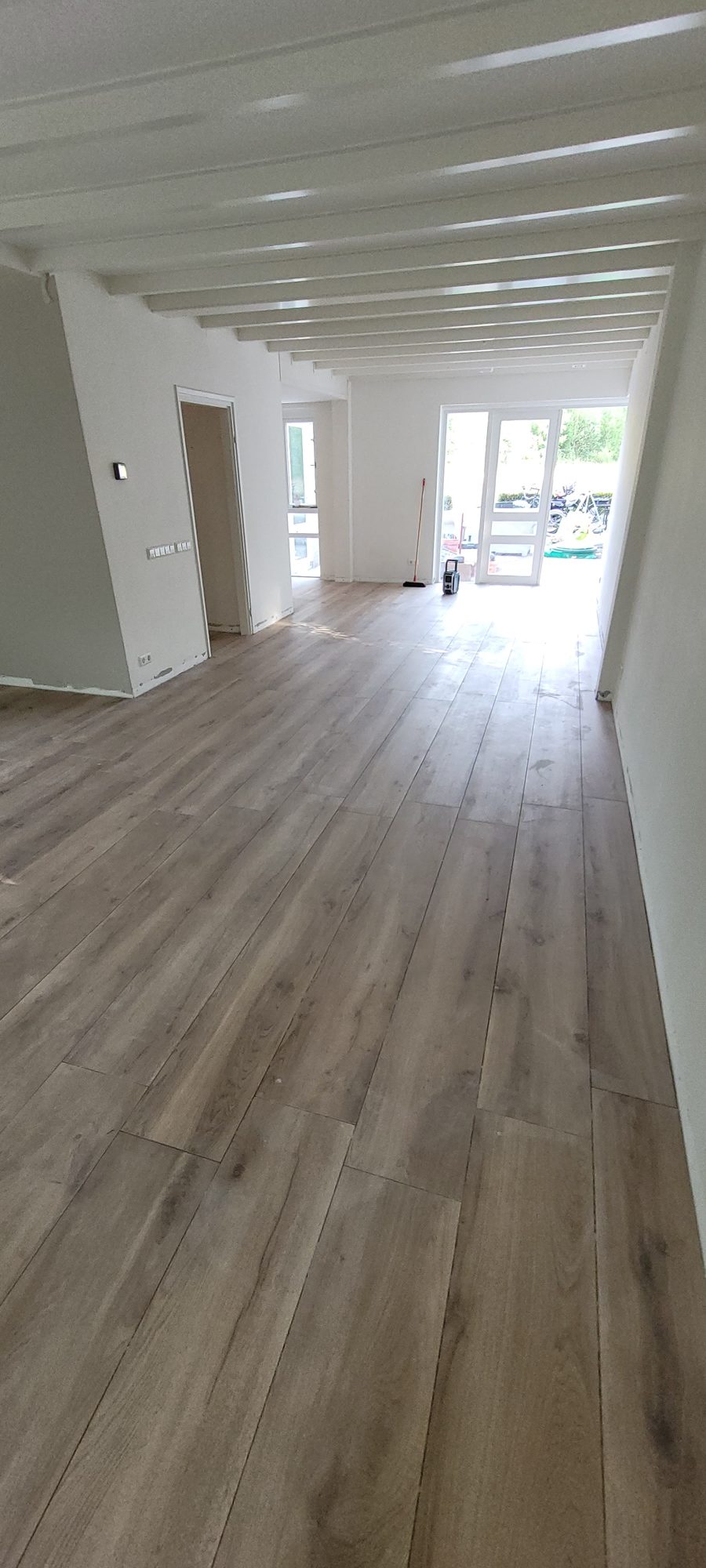 Lange woonkamer met een houtlook vloer en een balkenplafond