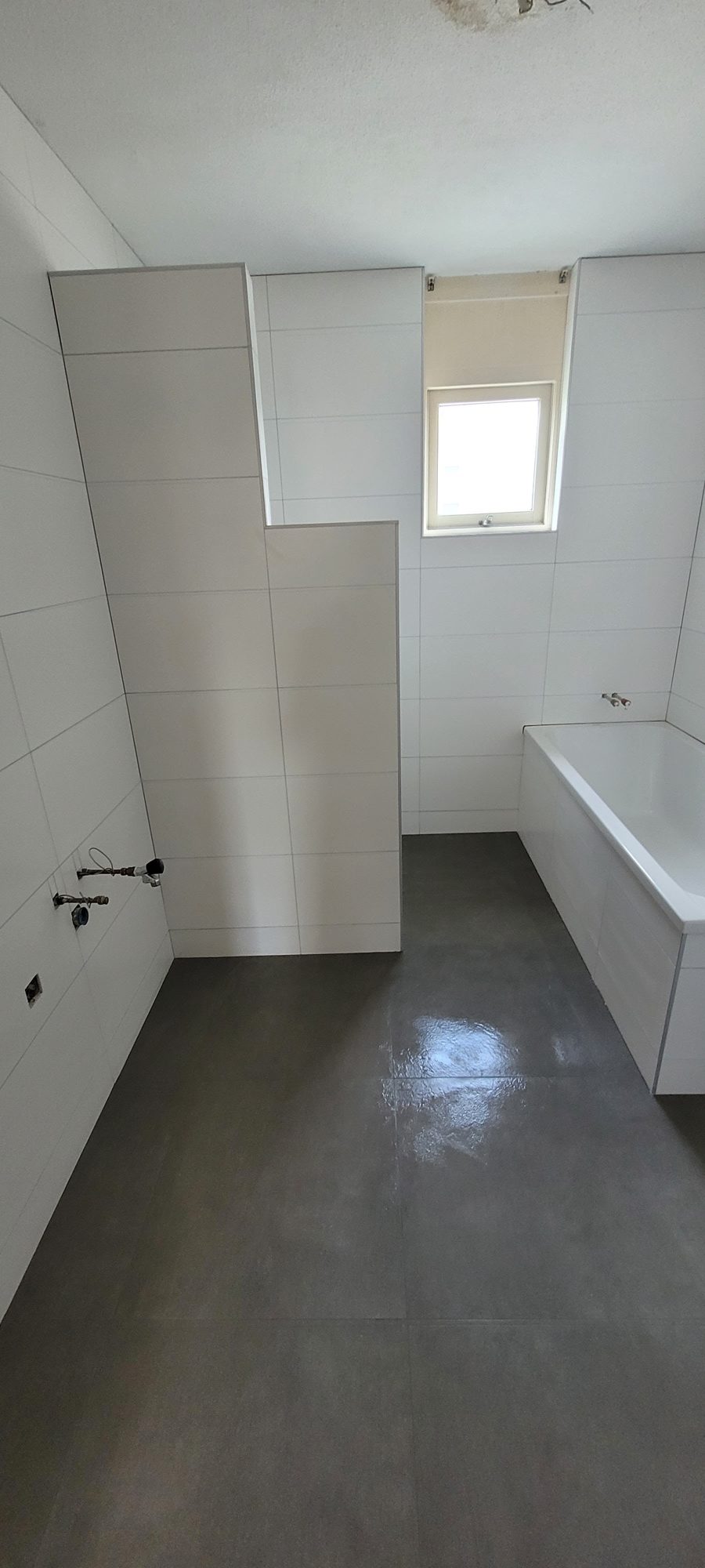 Badkamer onder een dakkapel met witte wandtegels, grote donkere vloertegels en een bad