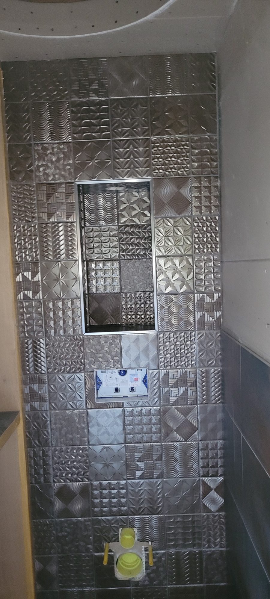 Toiletwand vol zilverkleurige 3D-patroontegels met een nis in het midden