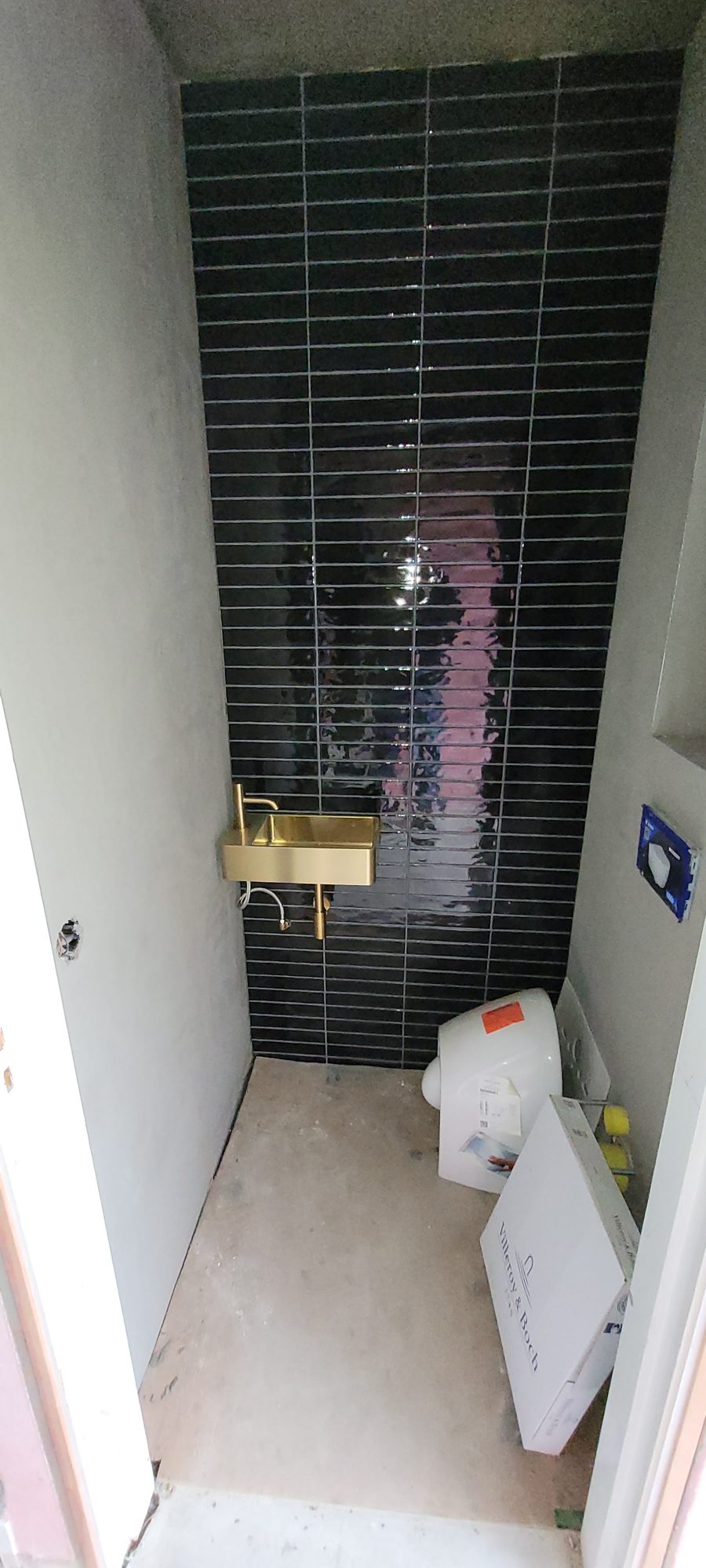 Toilet met donkere glanzende staafjestegels en een gouden fonteintje, nog in afbouw